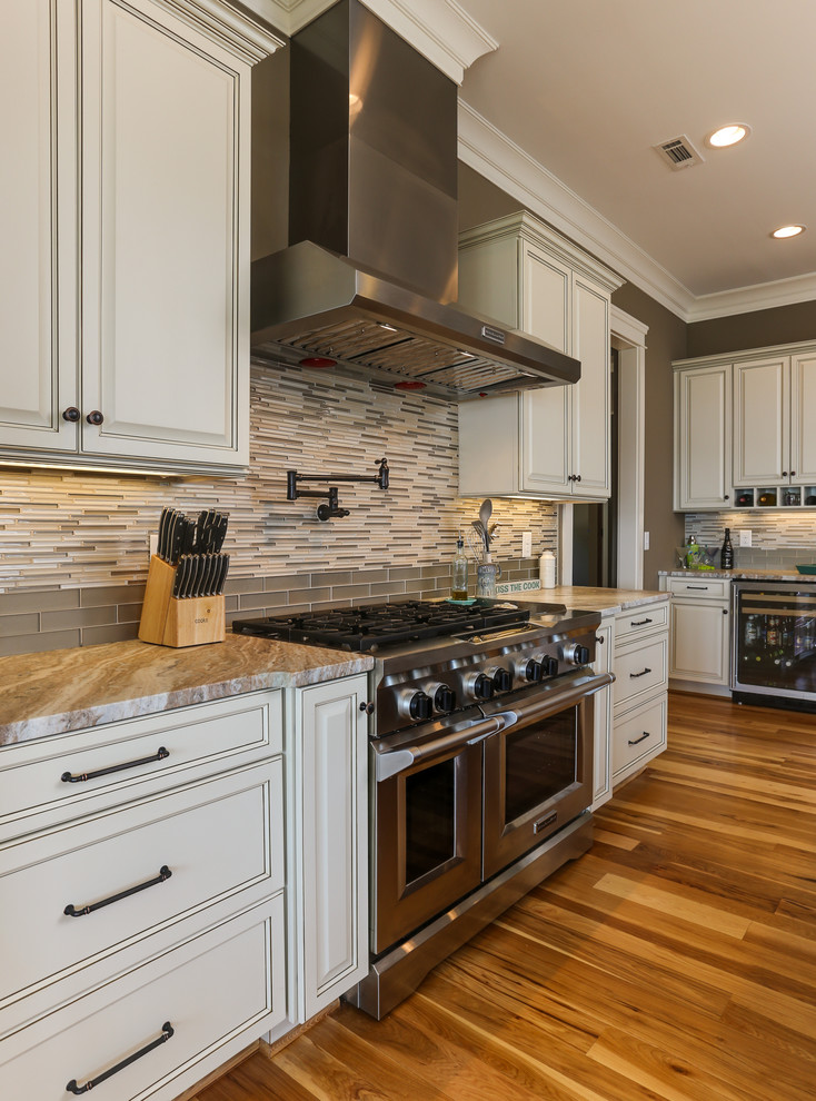 Kitchen - large traditional u-shaped medium tone wood floor kitchen idea in Raleigh with an undermount sink, recessed-panel cabinets, white cabinets, marble countertops, beige backsplash, glass tile backsplash, stainless steel appliances and an island
