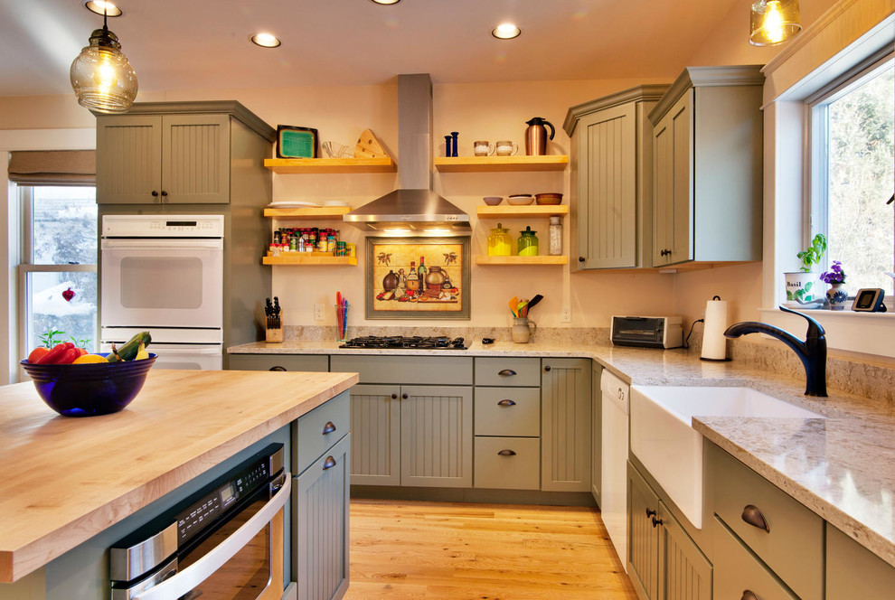 Example of a mid-sized arts and crafts l-shaped medium tone wood floor and brown floor kitchen design in Other with a farmhouse sink, shaker cabinets, green cabinets, white appliances, an island and beige countertops
