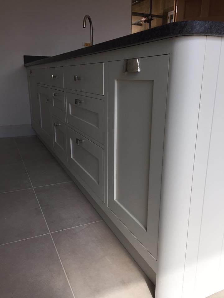 Photo of a medium sized contemporary galley kitchen/diner in Wiltshire with an integrated sink, recessed-panel cabinets, white cabinets, granite worktops, white splashback, cement tile splashback, black appliances, ceramic flooring, an island and beige floors.
