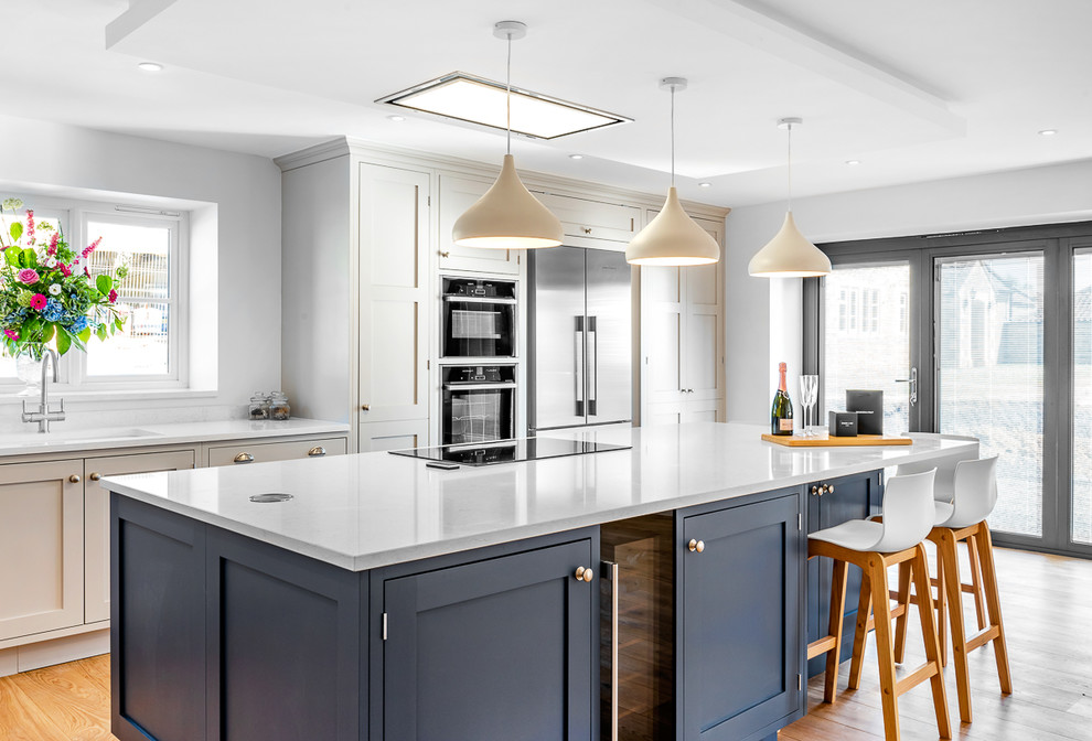 Esempio di una cucina design di medie dimensioni con ante con riquadro incassato, elettrodomestici in acciaio inossidabile, parquet chiaro, pavimento beige e top bianco