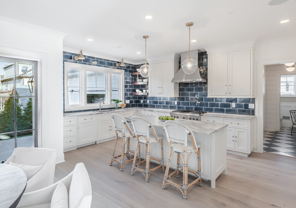 Photo of a beach style l-shaped kitchen/diner in New York with shaker cabinets, white cabinets, blue splashback, metro tiled splashback, stainless steel appliances, light hardwood flooring, an island and beige floors.