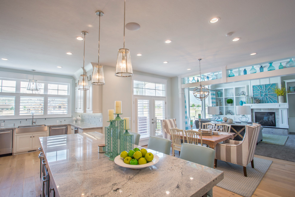 Inspiration for a coastal u-shaped light wood floor eat-in kitchen remodel in Salt Lake City with a farmhouse sink, shaker cabinets, white cabinets, granite countertops, white backsplash, glass tile backsplash, stainless steel appliances and an island