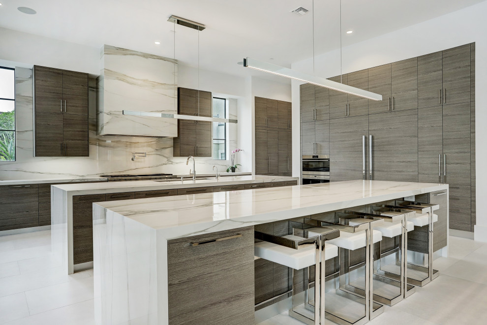Geräumige Moderne Küche in grau-weiß in L-Form mit Unterbauwaschbecken, flächenbündigen Schrankfronten, hellbraunen Holzschränken, Küchenrückwand in Grau, Elektrogeräten mit Frontblende, zwei Kücheninseln, grauem Boden und grauer Arbeitsplatte in Houston
