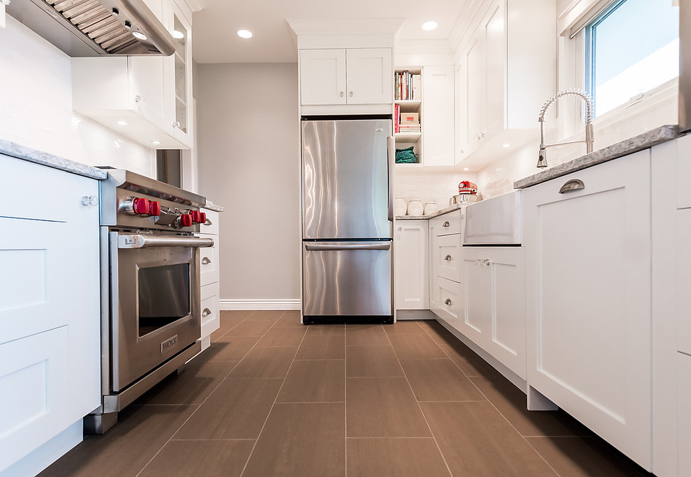 Design ideas for a medium sized traditional galley kitchen/diner in Vancouver with a belfast sink, shaker cabinets, white cabinets, engineered stone countertops, white splashback, metro tiled splashback, stainless steel appliances, porcelain flooring and no island.
