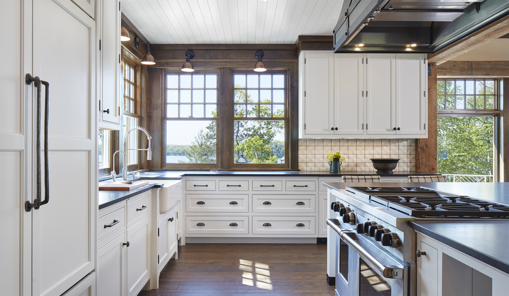 Inspiration for a large coastal l-shaped open plan kitchen in Minneapolis with white cabinets, white splashback, porcelain splashback, integrated appliances, medium hardwood flooring, an island, a belfast sink, shaker cabinets, composite countertops and brown floors.