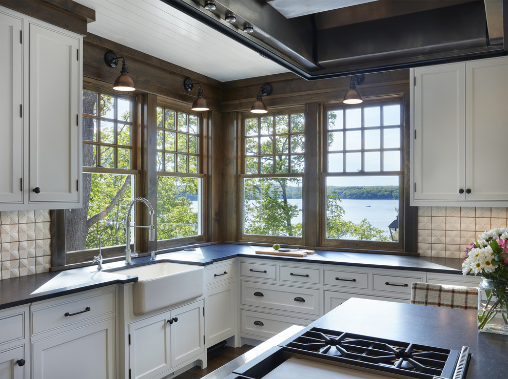 Inspiration for a large nautical l-shaped open plan kitchen in Minneapolis with white cabinets, white splashback, porcelain splashback, integrated appliances, medium hardwood flooring, an island, a belfast sink, shaker cabinets, composite countertops and brown floors.