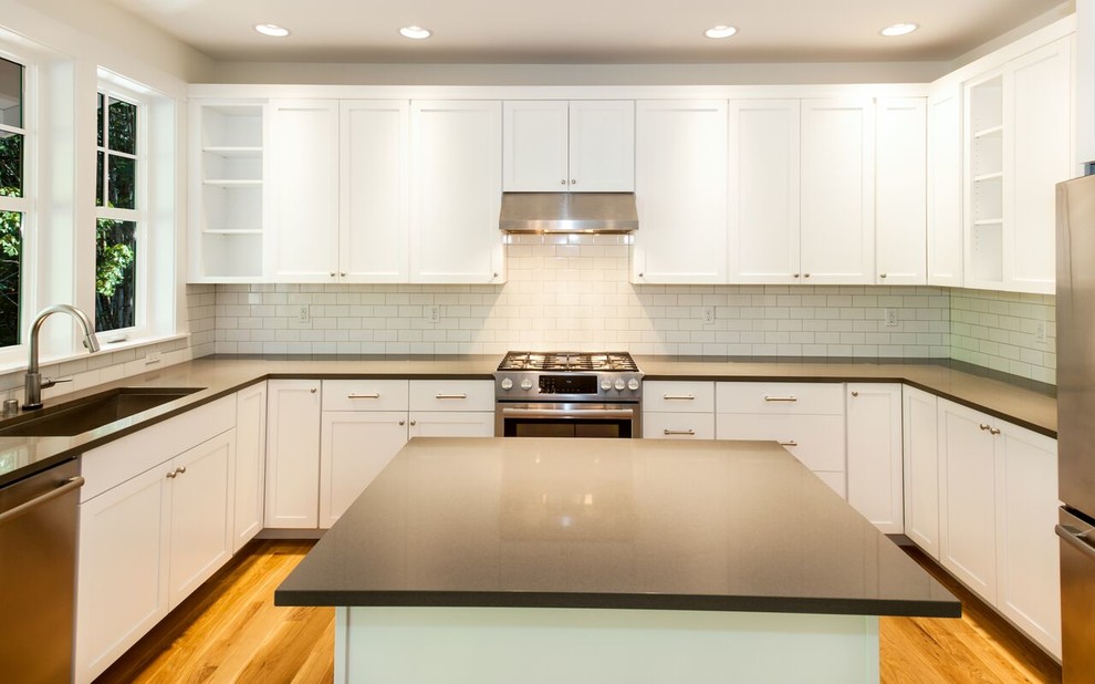 Mid-sized transitional u-shaped dark wood floor and brown floor open concept kitchen photo in Seattle with an undermount sink, beaded inset cabinets, white cabinets, white backsplash, stainless steel appliances, an island, solid surface countertops and subway tile backsplash