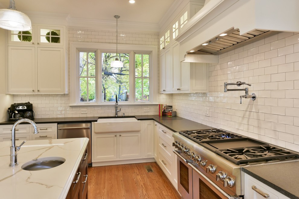 Large ornate l-shaped medium tone wood floor enclosed kitchen photo in New York with a farmhouse sink, beaded inset cabinets, white cabinets, quartz countertops, white backsplash, ceramic backsplash, stainless steel appliances and an island
