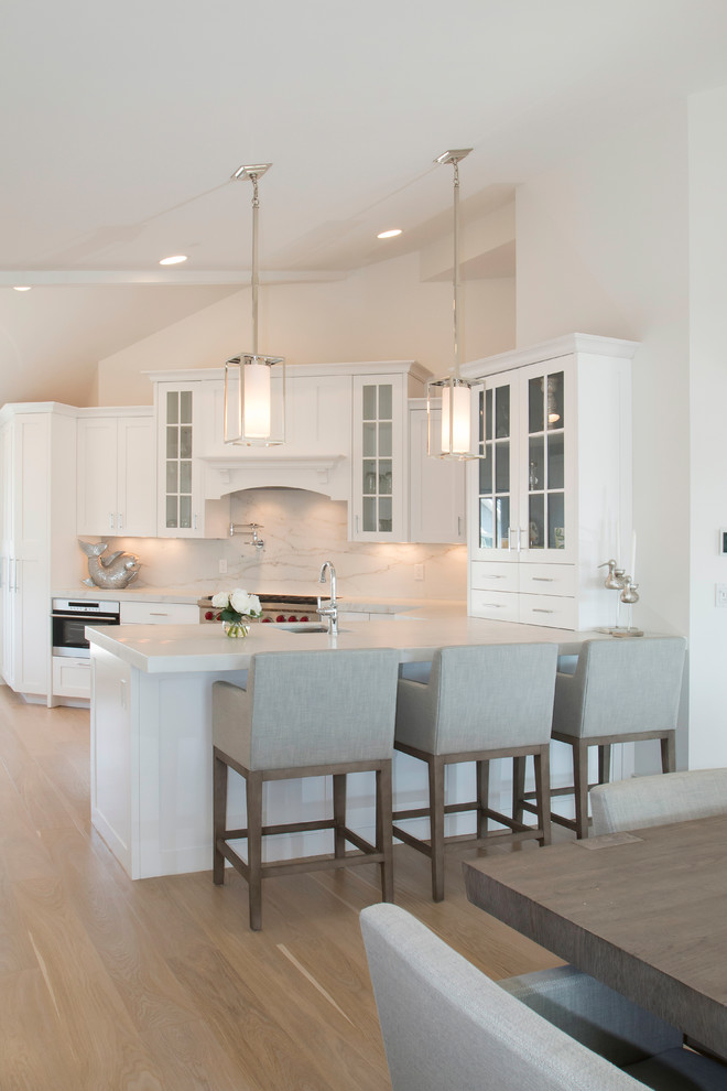Inspiration for a large coastal u-shaped light wood floor open concept kitchen remodel in New York with recessed-panel cabinets, white cabinets, marble countertops, paneled appliances, an island, an undermount sink, white backsplash and stone slab backsplash