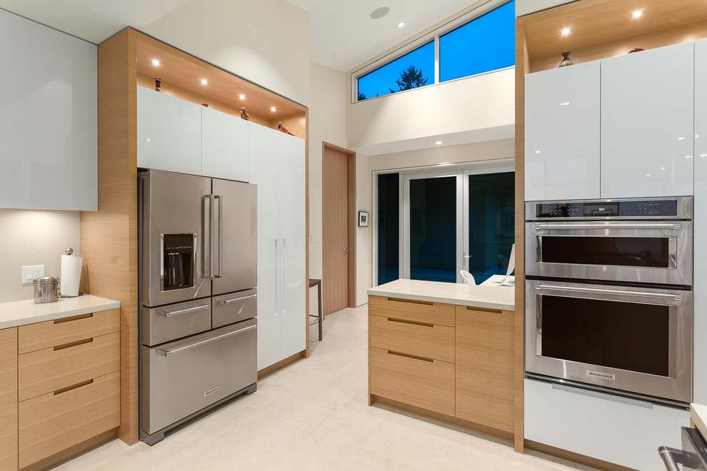 Modern inredning av ett stort kök, med en undermonterad diskho, släta luckor, skåp i ljust trä, granitbänkskiva, beige stänkskydd, rostfria vitvaror, kalkstensgolv och en halv köksö