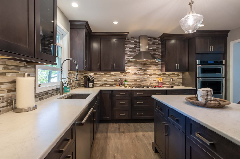 Inspiration for a large transitional l-shaped medium tone wood floor and brown floor eat-in kitchen remodel in Philadelphia with an undermount sink, recessed-panel cabinets, dark wood cabinets, quartz countertops, multicolored backsplash, porcelain backsplash, stainless steel appliances, an island and white countertops