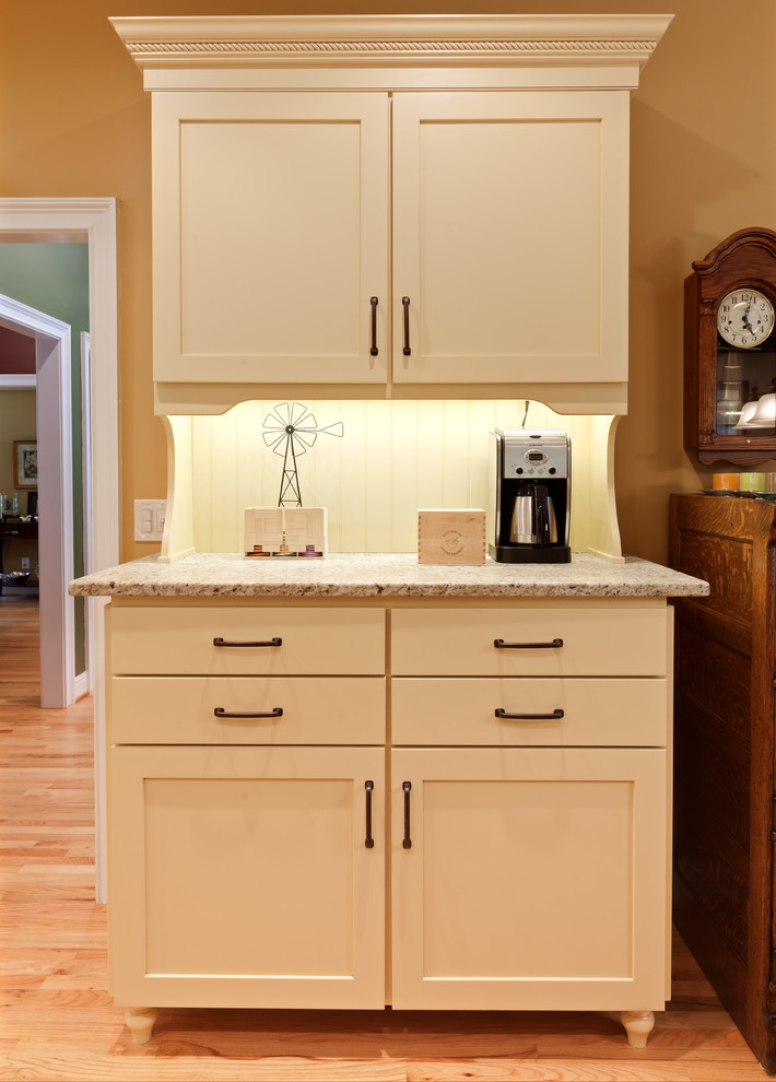 Inredning av ett klassiskt mellanstort beige beige kök, med en rustik diskho, skåp i shakerstil, gula skåp, granitbänkskiva, vitt stänkskydd, stänkskydd i porslinskakel, rostfria vitvaror, mellanmörkt trägolv, en köksö och brunt golv