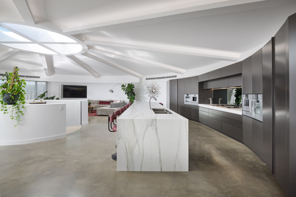 Expansive contemporary galley kitchen in Perth with a double-bowl sink, flat-panel cabinets, tile countertops, concrete flooring, an island, grey floors, grey cabinets, stainless steel appliances, white worktops and exposed beams.