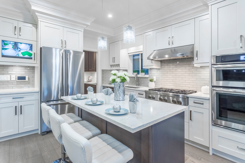 Example of a transitional l-shaped gray floor kitchen design in Vancouver with an undermount sink, shaker cabinets, white cabinets, white backsplash, stainless steel appliances and an island