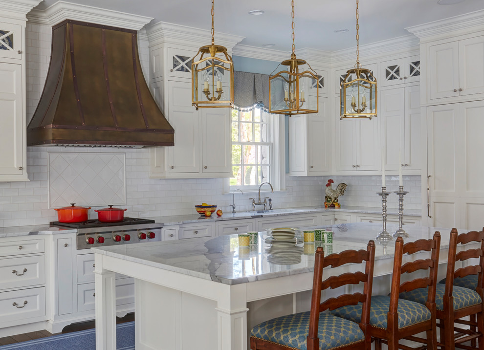 Klassisk inredning av ett stort vit vitt kök, med en undermonterad diskho, luckor med infälld panel, vita skåp, marmorbänkskiva, vitt stänkskydd, stänkskydd i keramik, rostfria vitvaror, mörkt trägolv, en köksö och brunt golv
