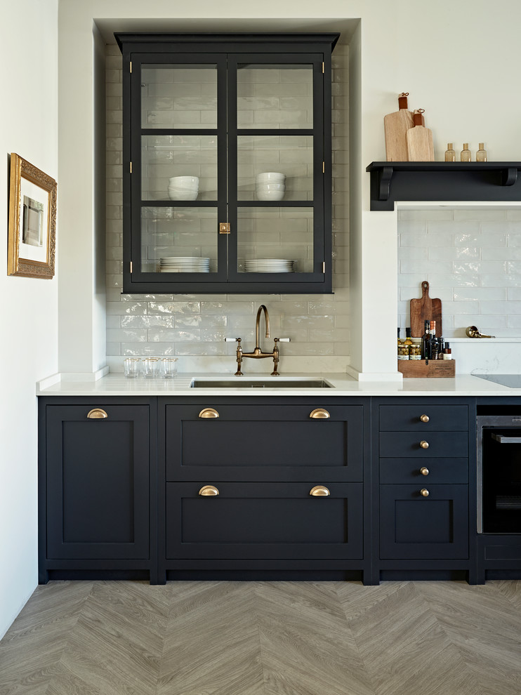Inspiration for a victorian single-wall kitchen/diner in Surrey with a submerged sink, shaker cabinets, blue cabinets, composite countertops, white splashback, metro tiled splashback, black appliances, light hardwood flooring, beige floors and white worktops.