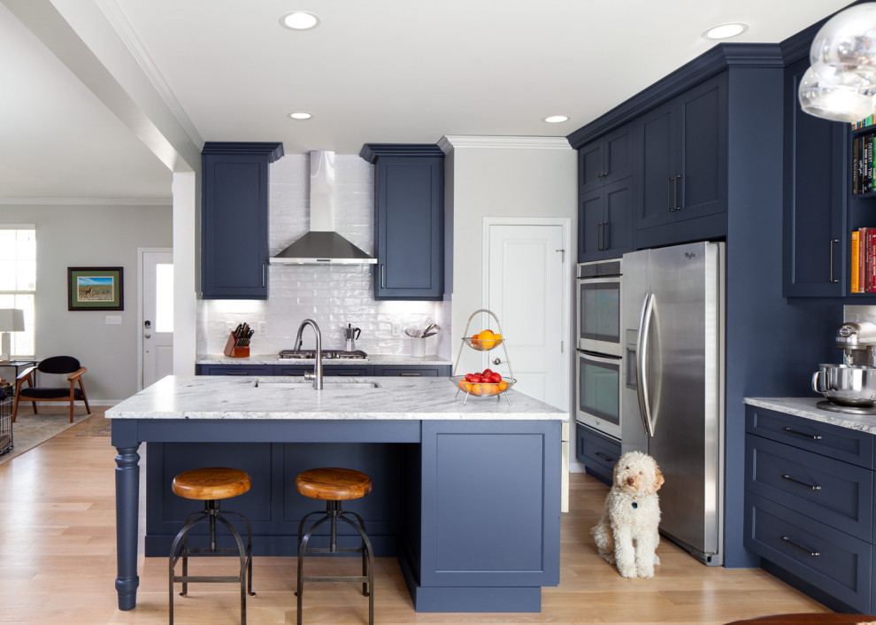 Example of a mid-sized transitional l-shaped medium tone wood floor and brown floor eat-in kitchen design in Raleigh with an undermount sink, recessed-panel cabinets, blue cabinets, granite countertops, white backsplash, ceramic backsplash, stainless steel appliances, an island and white countertops