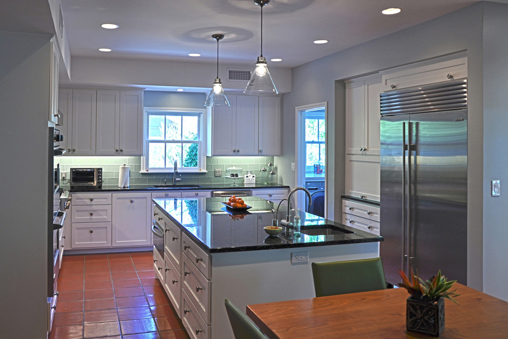 Inredning av ett modernt stort kök, med en undermonterad diskho, skåp i shakerstil, vita skåp, granitbänkskiva, grönt stänkskydd, stänkskydd i glaskakel, rostfria vitvaror, klinkergolv i terrakotta och en köksö