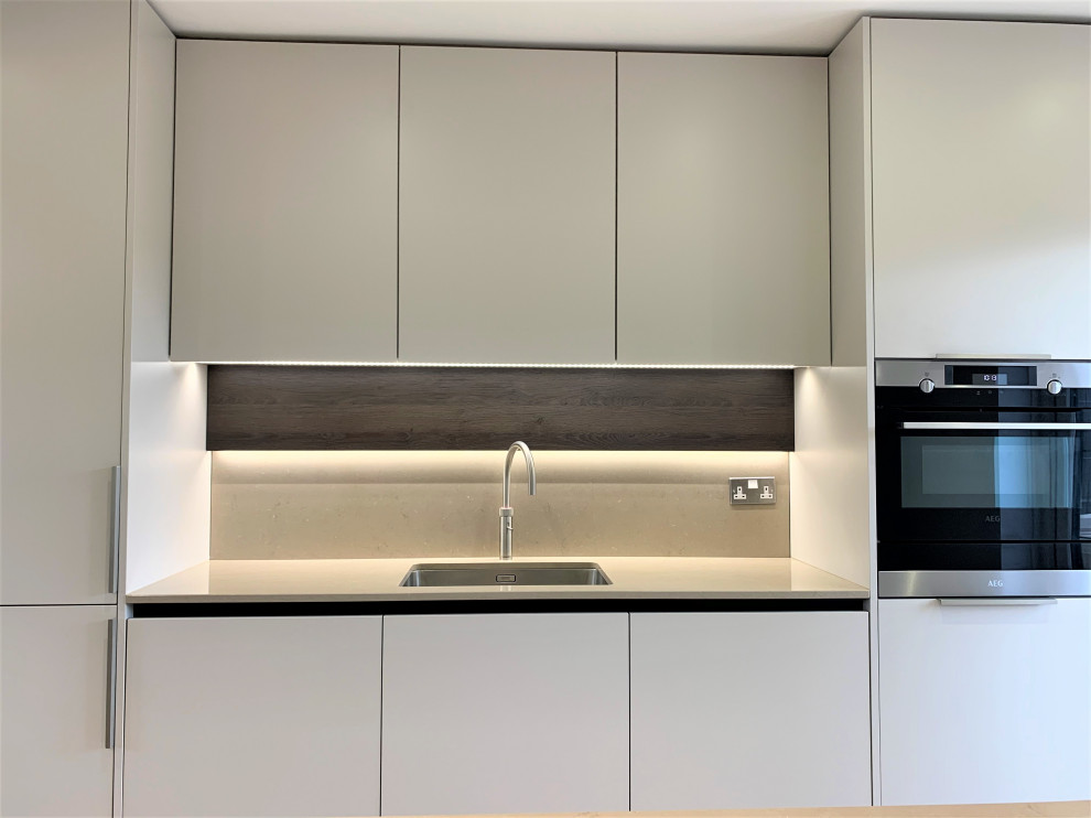 Medium sized contemporary single-wall kitchen/diner in Other with a single-bowl sink, flat-panel cabinets, medium wood cabinets, composite countertops, engineered quartz splashback, black appliances, vinyl flooring, an island and beige worktops.