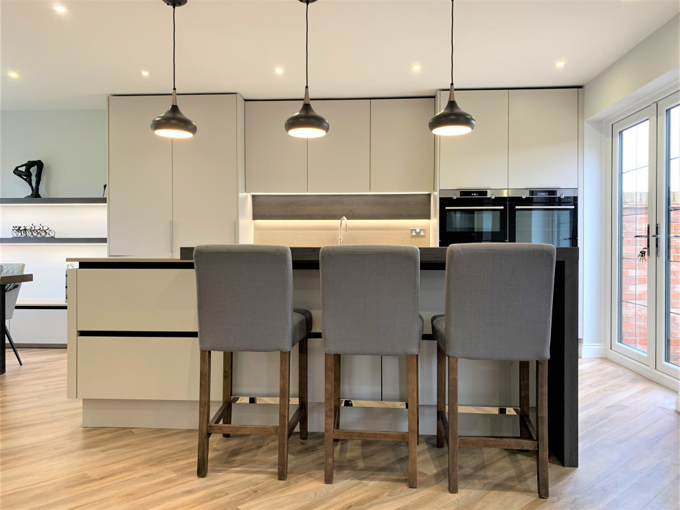 Medium sized contemporary single-wall kitchen/diner in Other with a single-bowl sink, flat-panel cabinets, medium wood cabinets, composite countertops, engineered quartz splashback, black appliances, vinyl flooring, an island and beige worktops.