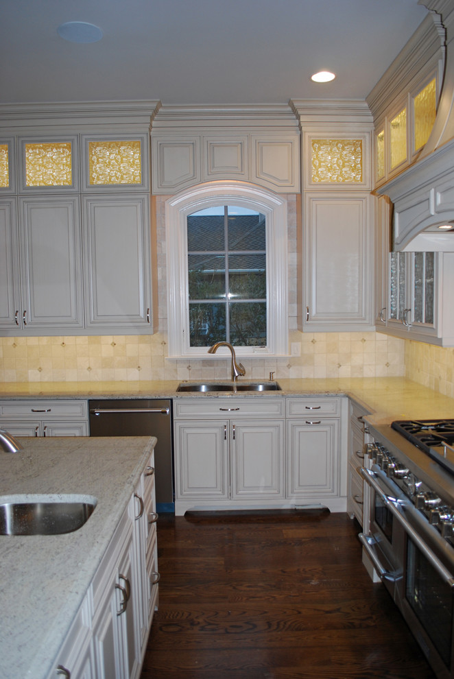 Photo of a medium sized classic l-shaped kitchen/diner in Wilmington with a submerged sink, raised-panel cabinets, white cabinets, beige splashback, stainless steel appliances, dark hardwood flooring and an island.