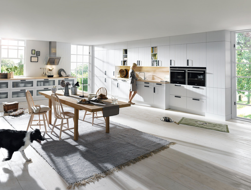 Geräumige Country Wohnküche mit weißen Schränken, Küchenrückwand in Beige, Küchengeräten aus Edelstahl und gebeiztem Holzboden in Surrey