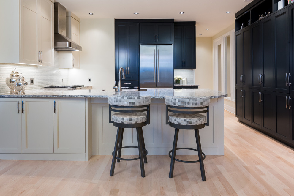 Inspiration for a medium sized contemporary u-shaped open plan kitchen in Ottawa with a belfast sink, recessed-panel cabinets, black cabinets, granite worktops, white splashback, glass tiled splashback, stainless steel appliances, light hardwood flooring and a breakfast bar.