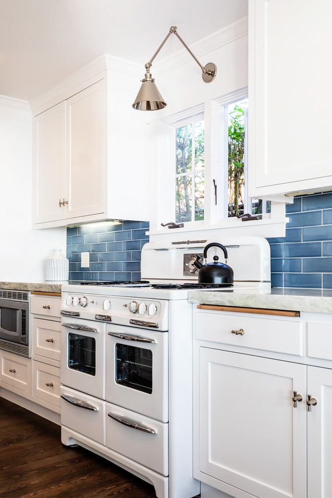 Foto på ett stort maritimt grå kök, med skåp i shakerstil, vita skåp, granitbänkskiva, blått stänkskydd, stänkskydd i keramik, mörkt trägolv, vita vitvaror och brunt golv