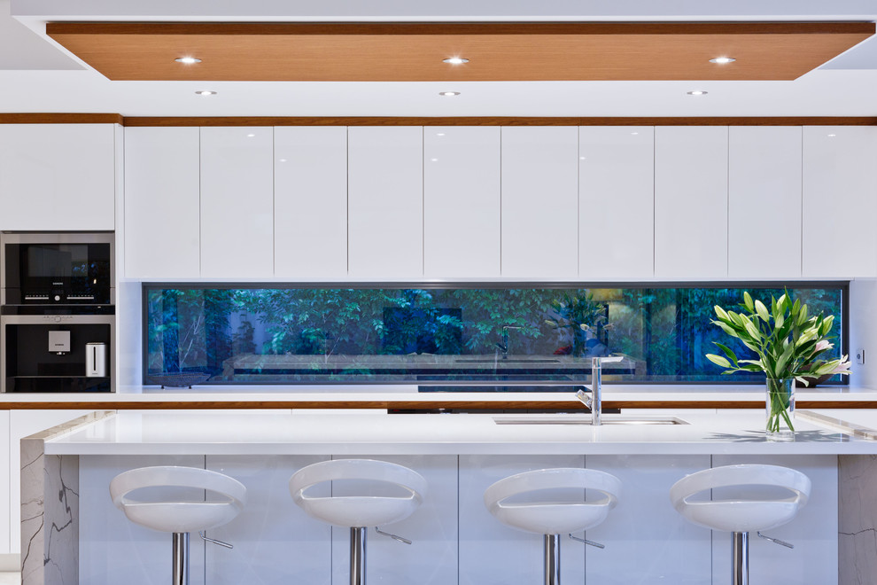Пример оригинального дизайна: параллельная кухня-гостиная у окна, среднего размера в современном стиле с врезной мойкой, плоскими фасадами, белыми фасадами, столешницей из кварцевого агломерата, техникой из нержавеющей стали, полом из керамической плитки, островом и серым полом
