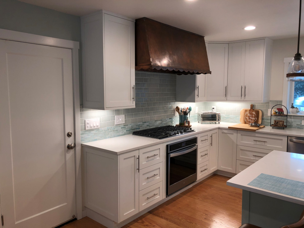 Klassisk inredning av ett stort vit vitt kök, med skåp i shakerstil, vita skåp, blått stänkskydd, stänkskydd i keramik, vita vitvaror, mellanmörkt trägolv, en köksö och brunt golv
