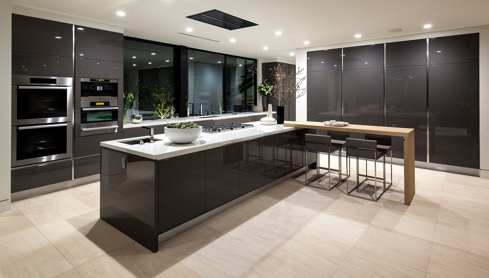 This is an example of a large contemporary l-shaped enclosed kitchen in Los Angeles with a submerged sink, glass-front cabinets, black cabinets, stainless steel appliances, porcelain flooring, an island, beige floors and white worktops.