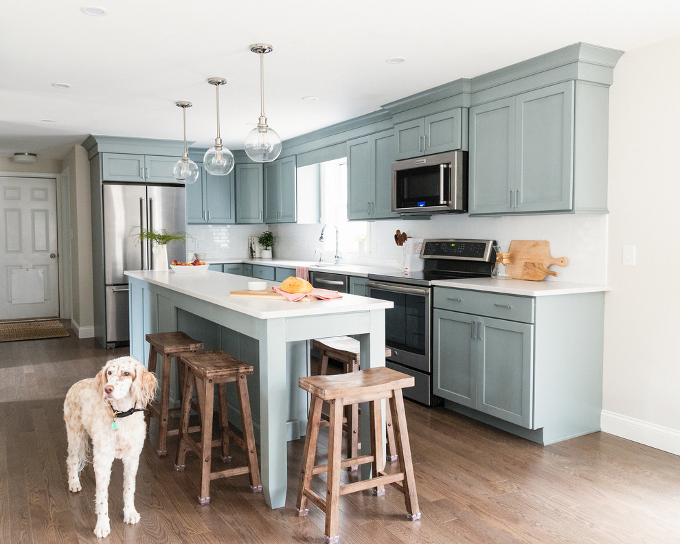 Bild på ett mellanstort vintage linjärt kök med öppen planlösning, med en undermonterad diskho, skåp i shakerstil, blå skåp, bänkskiva i kvarts, vitt stänkskydd, stänkskydd i keramik, rostfria vitvaror, mellanmörkt trägolv, en köksö och brunt golv