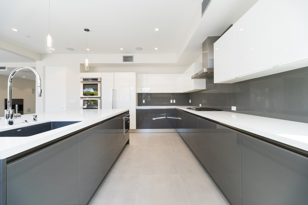This is an example of a large contemporary u-shaped kitchen in Los Angeles with a submerged sink, flat-panel cabinets, grey cabinets, quartz worktops, grey splashback, stone slab splashback, stainless steel appliances, porcelain flooring, an island, grey floors and white worktops.