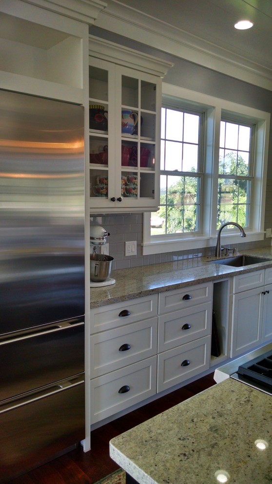 This is an example of a nautical kitchen in Hawaii with white cabinets, grey splashback, metro tiled splashback, stainless steel appliances, dark hardwood flooring and an island.