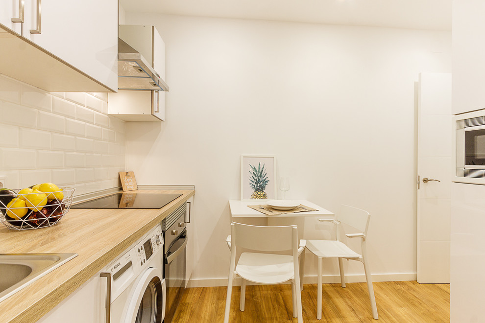 マドリードにある北欧スタイルのおしゃれなキッチン (フラットパネル扉のキャビネット、白いキャビネット、木材カウンター、白いキッチンパネル、サブウェイタイルのキッチンパネル、シルバーの調理設備、無垢フローリング) の写真