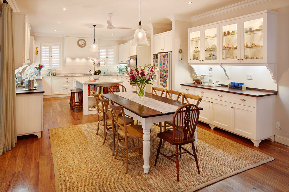 Große Klassische Wohnküche in U-Form mit Schrankfronten im Shaker-Stil, weißen Schränken, Küchenrückwand in Weiß, braunem Holzboden und Kücheninsel in Sonstige