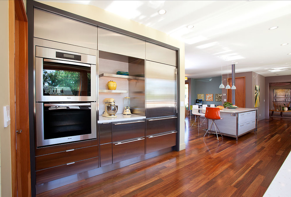 Bild på ett stort funkis kök, med rostfria vitvaror, släta luckor, skåp i rostfritt stål, en köksö, en undermonterad diskho, bänkskiva i kvarts, mellanmörkt trägolv och brunt golv