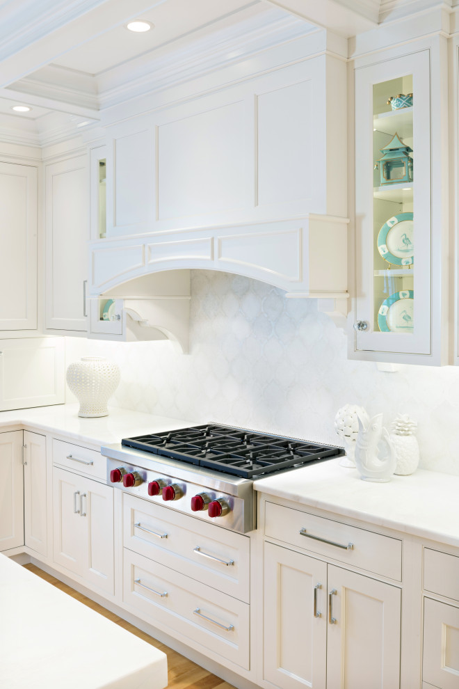 Inredning av ett klassiskt stort vit vitt kök, med en undermonterad diskho, luckor med profilerade fronter, vita skåp, bänkskiva i kvartsit, vitt stänkskydd, stänkskydd i marmor, integrerade vitvaror, ljust trägolv och en köksö