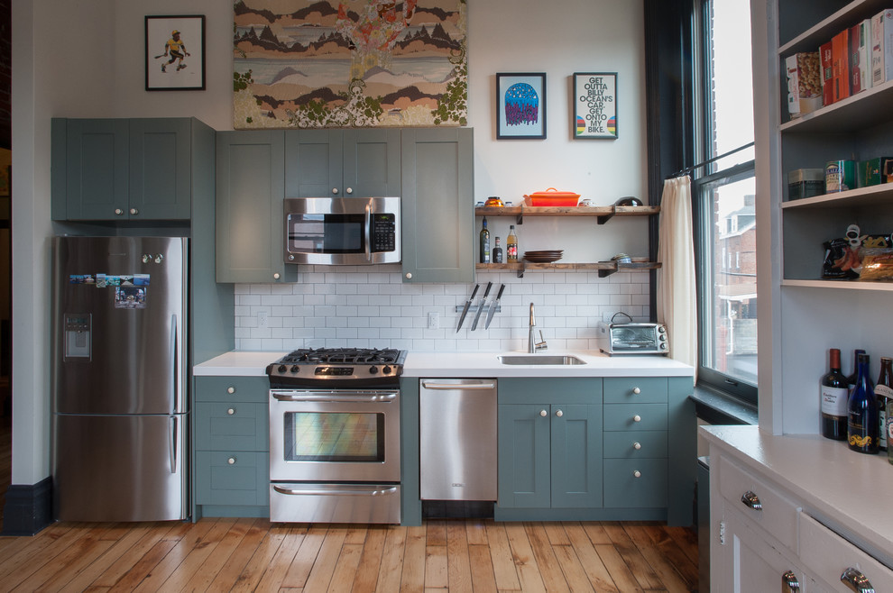 Réalisation d'une cuisine linéaire design avec un électroménager en acier inoxydable, des portes de placard bleues, une crédence blanche, une crédence en carrelage métro et un placard à porte shaker.