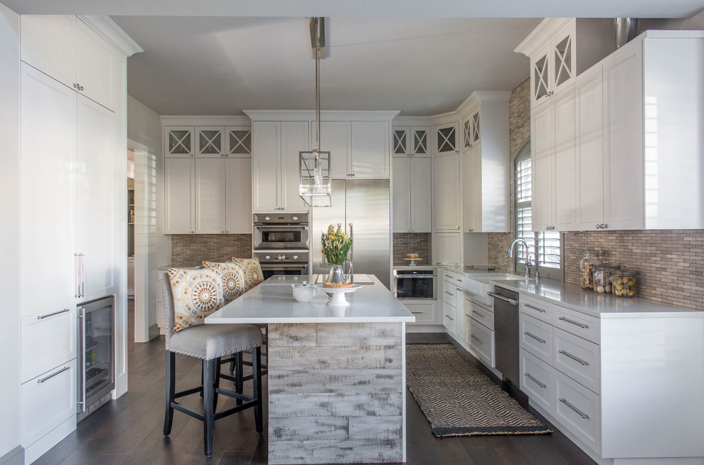 Large classic kitchen in Austin with a belfast sink, shaker cabinets, white cabinets, engineered stone countertops, grey splashback, stone tiled splashback, stainless steel appliances, dark hardwood flooring and an island.