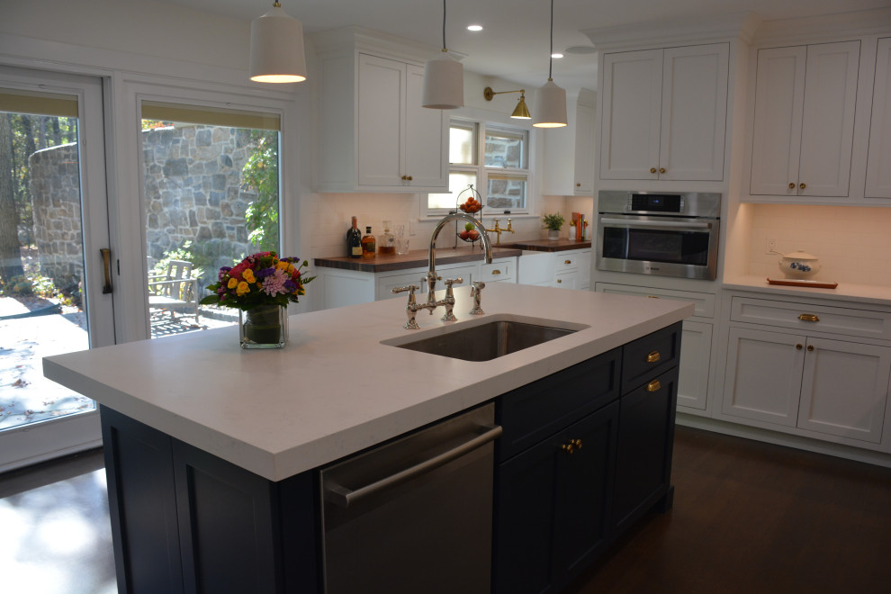Bild på ett stort vintage flerfärgad flerfärgat kök, med en undermonterad diskho, skåp i shakerstil, vita skåp, bänkskiva i kvarts, vitt stänkskydd, stänkskydd i porslinskakel, rostfria vitvaror, klinkergolv i porslin, en köksö och brunt golv