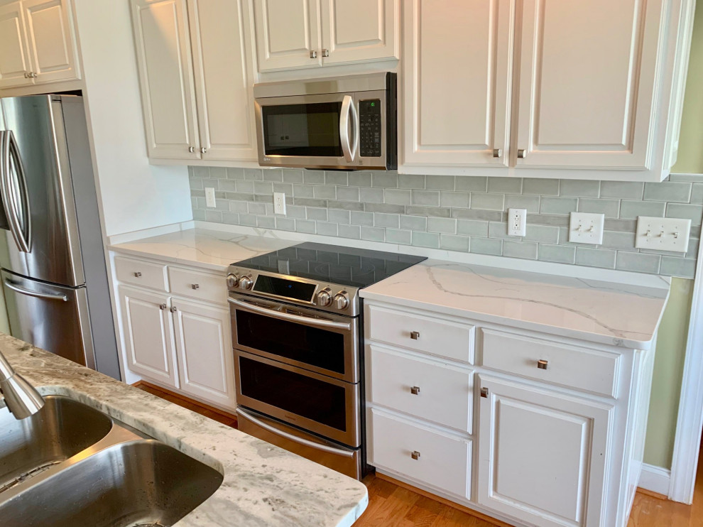 Photo of a medium sized nautical kitchen/diner in Wilmington with a double-bowl sink, raised-panel cabinets, white cabinets, green splashback, porcelain splashback, stainless steel appliances, medium hardwood flooring and an island.