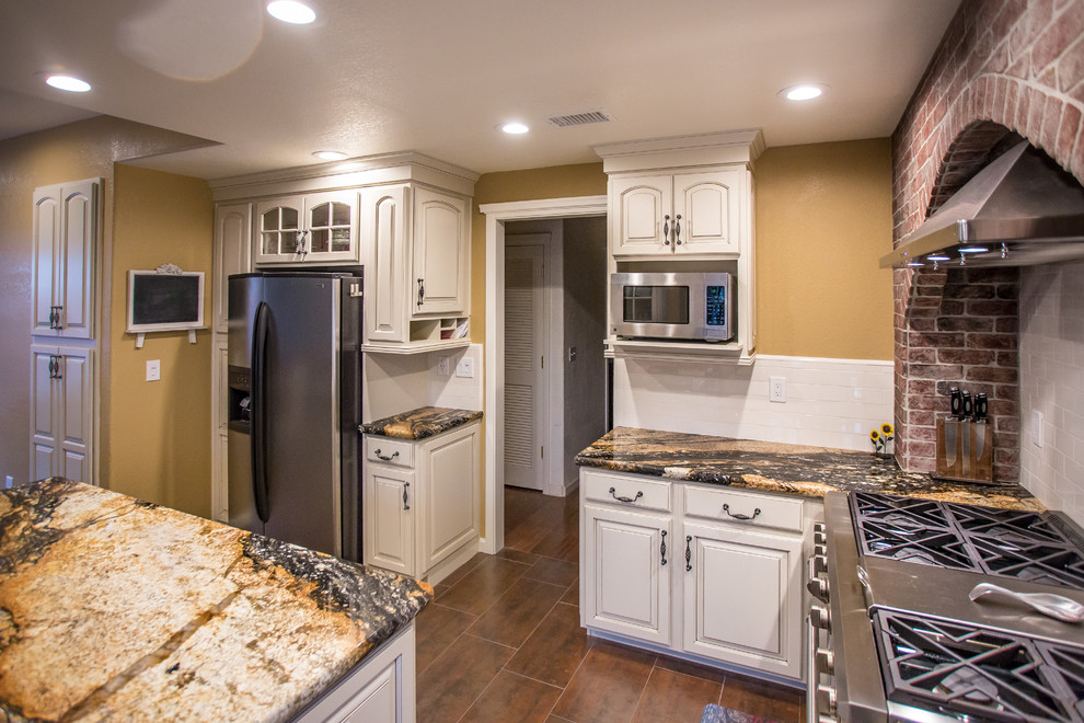 Exempel på ett klassiskt u-kök, med en rustik diskho, luckor med upphöjd panel, skåp i slitet trä, granitbänkskiva, vitt stänkskydd, stänkskydd i tunnelbanekakel, rostfria vitvaror, klinkergolv i porslin, en köksö och brunt golv