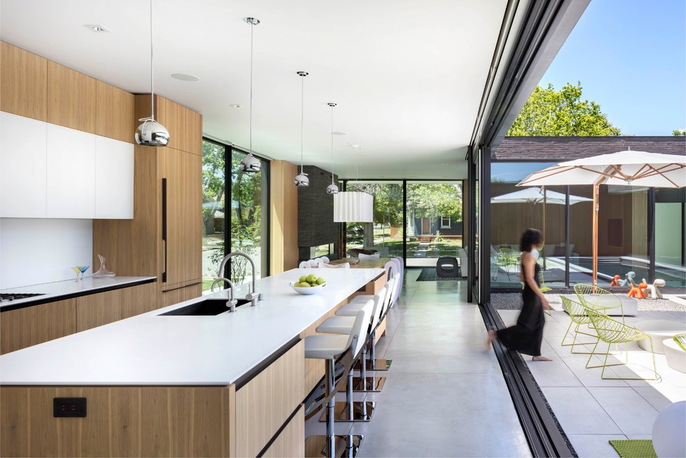 Cette photo montre une cuisine ouverte parallèle et encastrable moderne en bois clair avec un évier encastré, un placard à porte plane, une crédence blanche, sol en béton ciré, îlot, un sol gris et un plan de travail blanc.