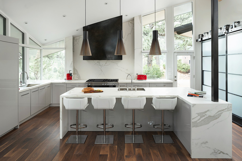 Minimalist l-shaped dark wood floor and brown floor kitchen photo in Denver with an undermount sink, flat-panel cabinets, gray cabinets, solid surface countertops, white backsplash, stone slab backsplash, paneled appliances, an island and white countertops