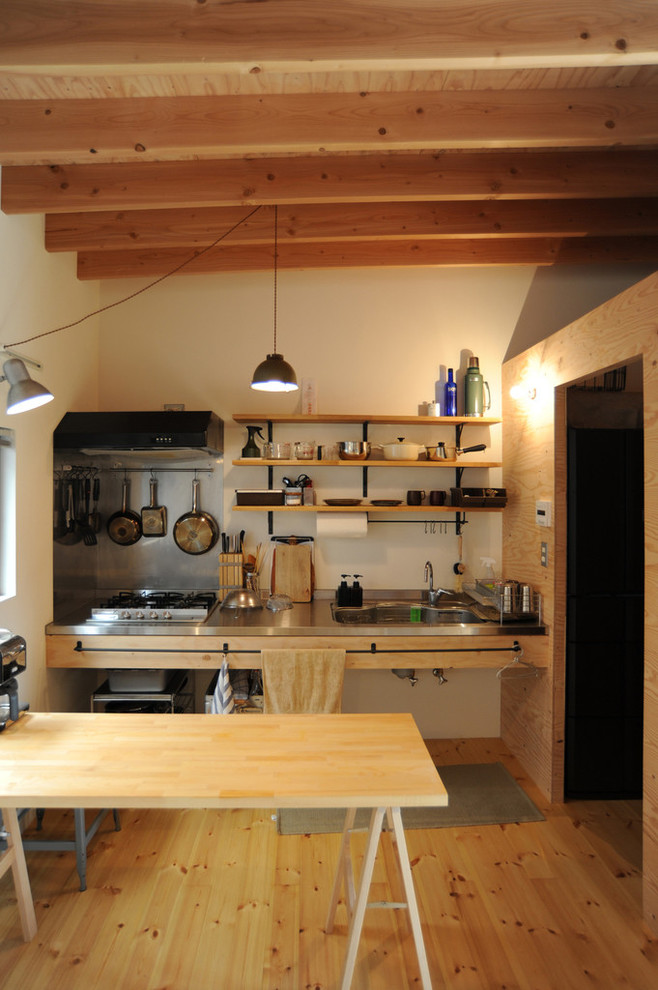 Foto på ett funkis linjärt kök med öppen planlösning, med en undermonterad diskho, öppna hyllor, skåp i ljust trä, bänkskiva i rostfritt stål, stänkskydd med metallisk yta, rostfria vitvaror och ljust trägolv