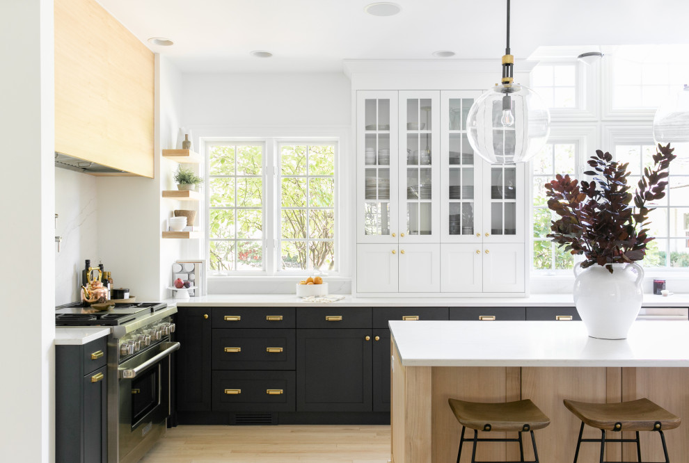 Photo of a traditional l-shaped kitchen in Chicago with shaker cabinets, black cabinets, stainless steel appliances, light hardwood flooring, an island, beige floors and white worktops.