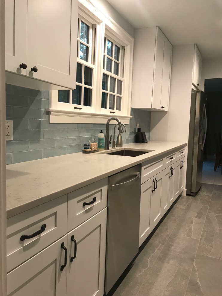 Bild på ett mellanstort vintage vit vitt kök, med en undermonterad diskho, luckor med infälld panel, vita skåp, bänkskiva i kvartsit, blått stänkskydd, stänkskydd i glaskakel, rostfria vitvaror, klinkergolv i porslin och grått golv