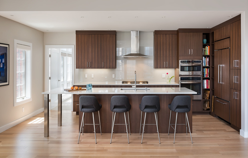 Example of a mid-sized trendy l-shaped light wood floor and beige floor kitchen design in Boston with flat-panel cabinets, dark wood cabinets, quartz countertops, gray backsplash, glass sheet backsplash, stainless steel appliances, an island, white countertops and an undermount sink