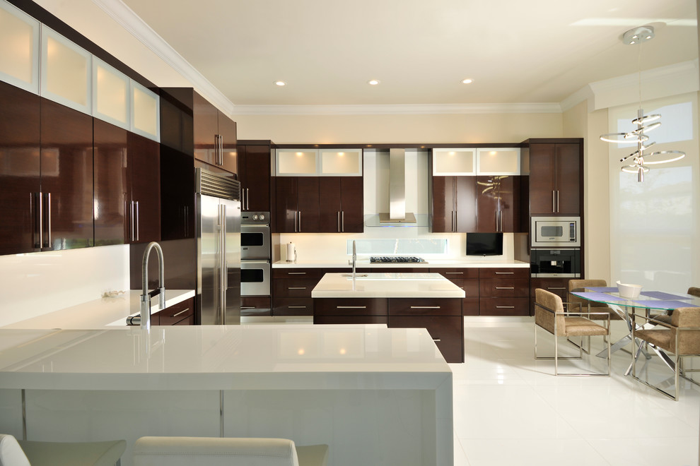 Large contemporary u-shaped open plan kitchen in Miami with flat-panel cabinets, dark wood cabinets, white splashback, glass sheet splashback, stainless steel appliances, ceramic flooring, an island, a submerged sink, composite countertops and white floors.